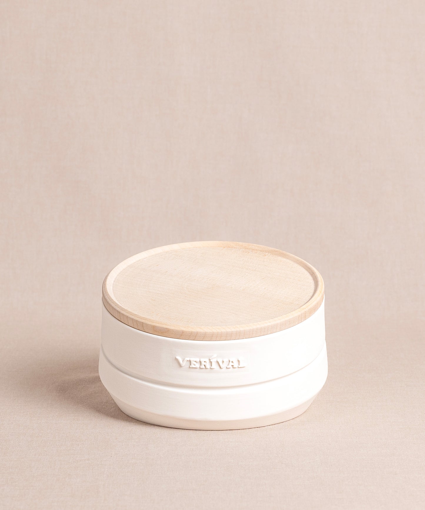 Auf einem beigen Untergrund steht ein runder, weißer Keramikbehälter von Verival Bio mit Ahornholzdeckel und seitliche Prägung „VERIVAL“. Er eignet sich perfekt für Aufbewahrung und Präsentation von Frühstücksgerichte wie Porridge, Granola oder Müsli.