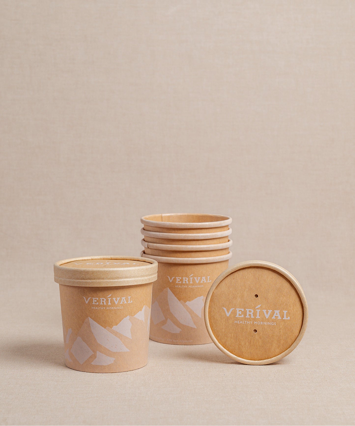 Gestapelte und einzelne To-Go-Becher mit Deckel von Verival Bio sind auf beigem Hintergrund platziert, ideal für Ihr Frühstück unterwegs.