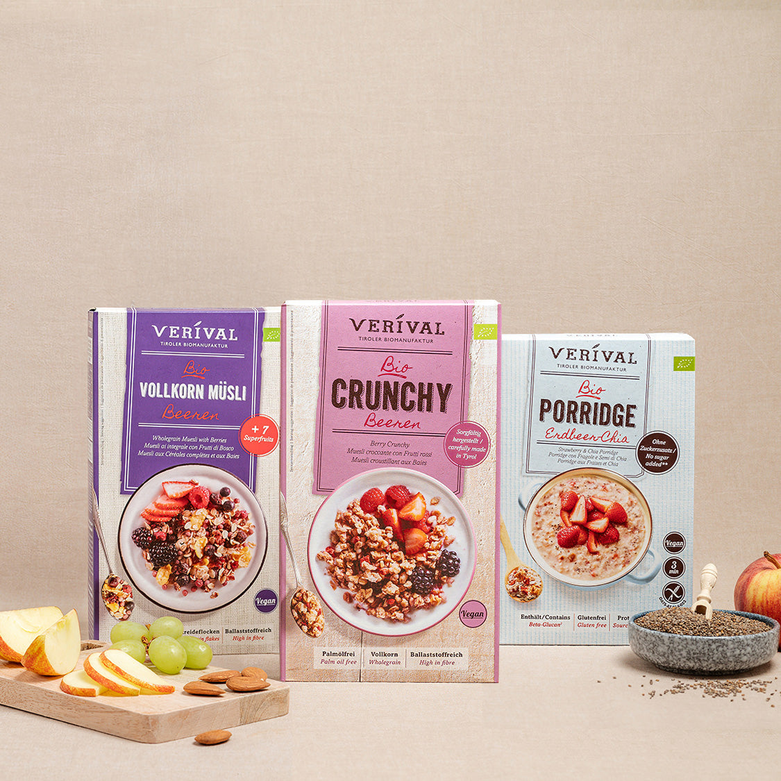 Drei Schachteln mit Verival-Müsliprodukten – Vollkorn Müsli, Crunchy Beeren und Porridge – werden auf einem neutralen Hintergrund mit Obst- und Müsli-Requisiten davor präsentiert.