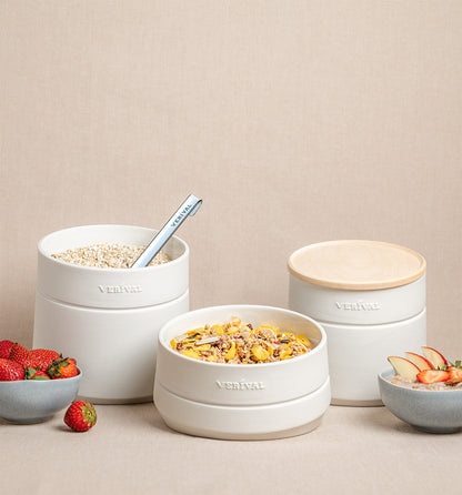 Verival Bio Frühstücksbehälter aus Porzellan für Porridge, Granola und Müsli mit Ahornholz-Deckel neben Schalen mit Erdbeeren, Apfelscheiben und einem Löffel.
